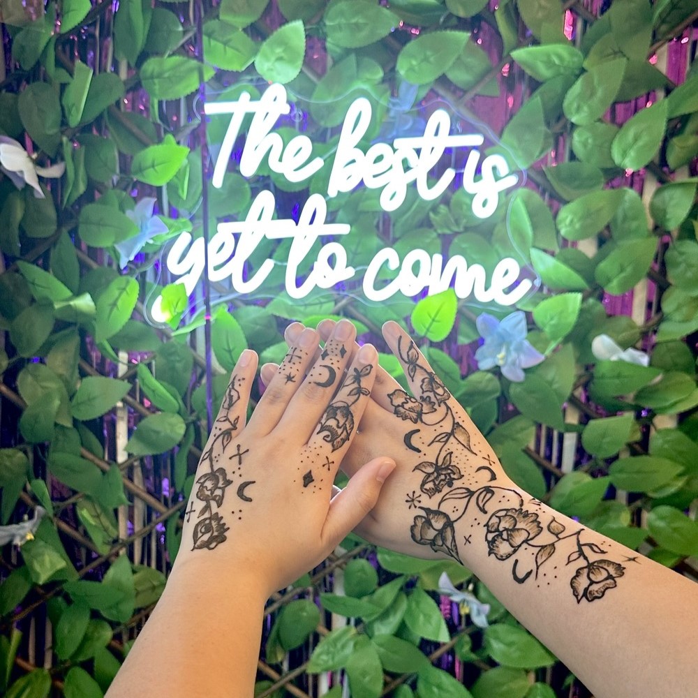 hands with henna tattoo design in front of an LED sign saying 